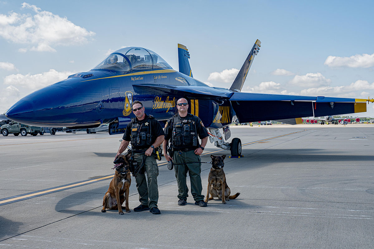 K9 Zuul poses next to his handler Deputy Castle. The two stand next to K9 Vero and his handler Capt. Debolt. All in front of a U.S. Navy Blue Angels plane.